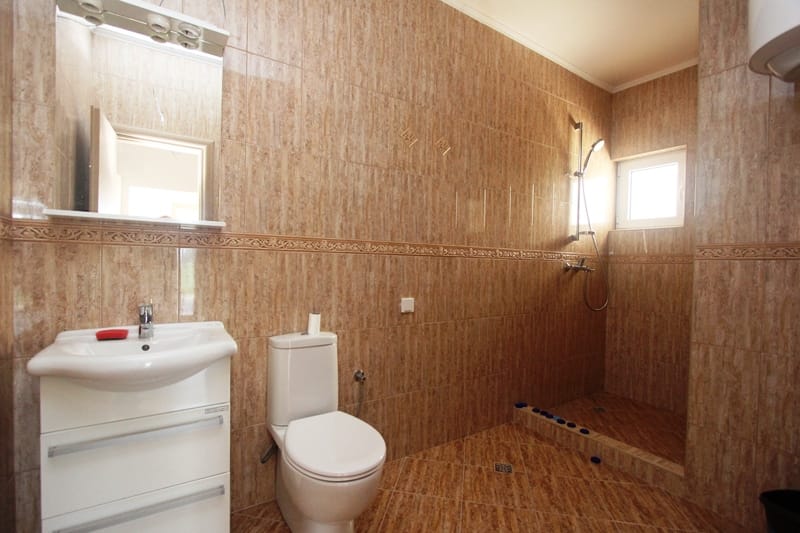 Bathroom with a shower cabin and white fixtures in a house for sale in Baošići, Montenegro, finished with beige tiles.