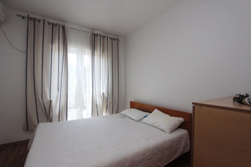 Bright bedroom with a double bed and curtains in a house in Baošići, Montenegro. Cozy interior with wooden furniture.