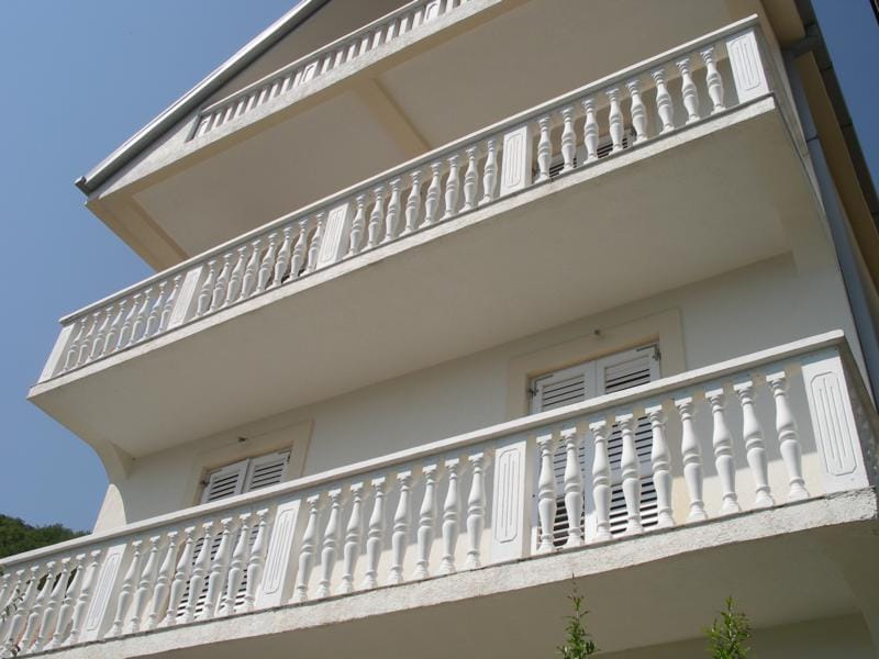 Fassade eines Hauses in Baošići, Montenegro: helle Wände und klassische weiße Balustraden an den zweistöckigen Balkonen.