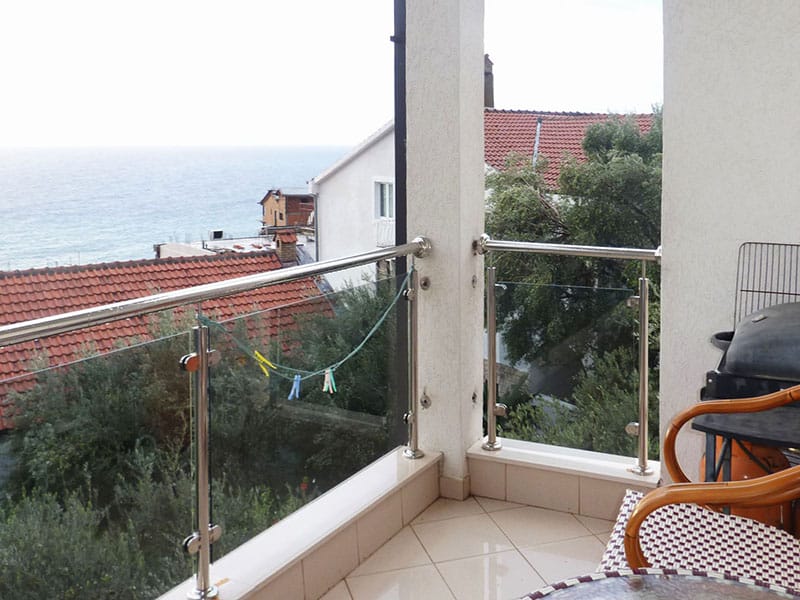 Balcony with a sea view in an apartment in Sveti Stefan, Montenegro: glass railings, tiled flooring, and patio furniture.