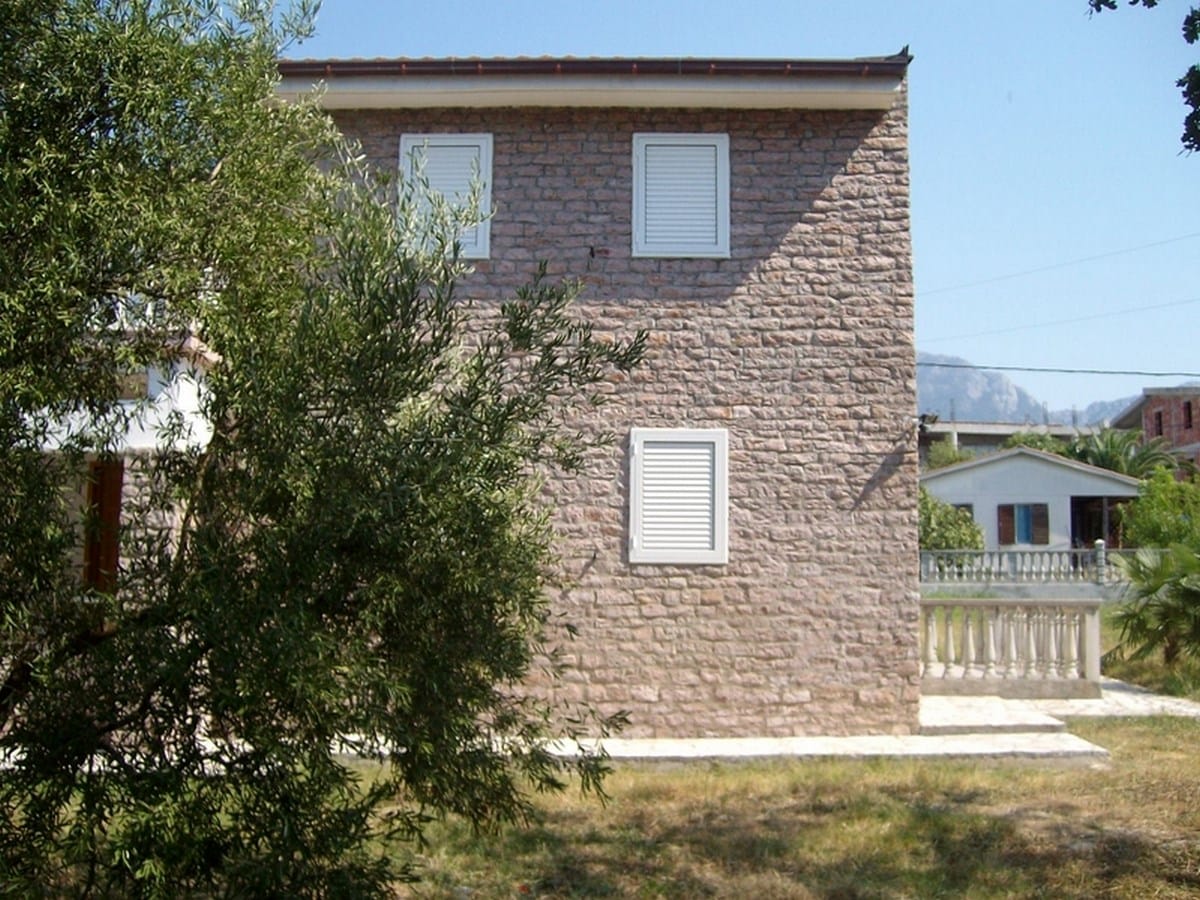 Dvospratna vila od prirodnog kamena sa belim kapcima u gradu Bar, Crna Gora, pogled na fasadu i baštu.