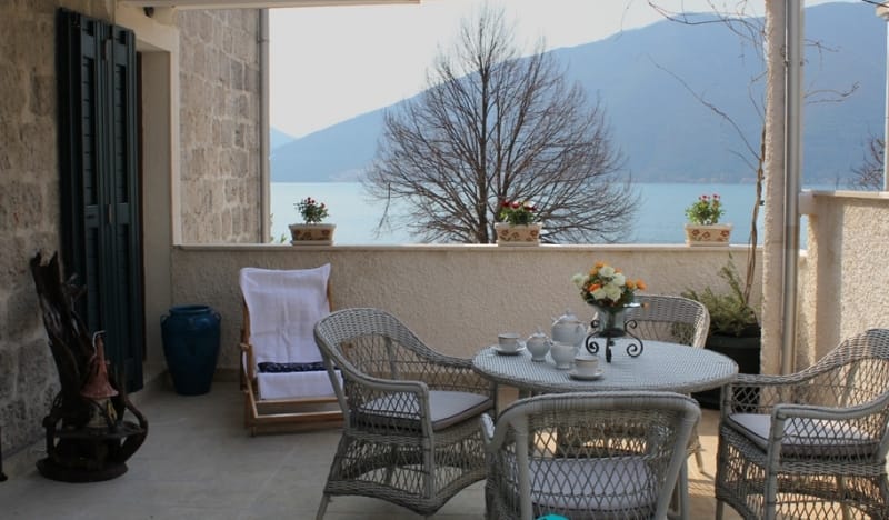 Терраса дома в Стрп, Черногория: плетеная мебель, вид на море и горы, каменная отделка стен и уютная зона отдыха.