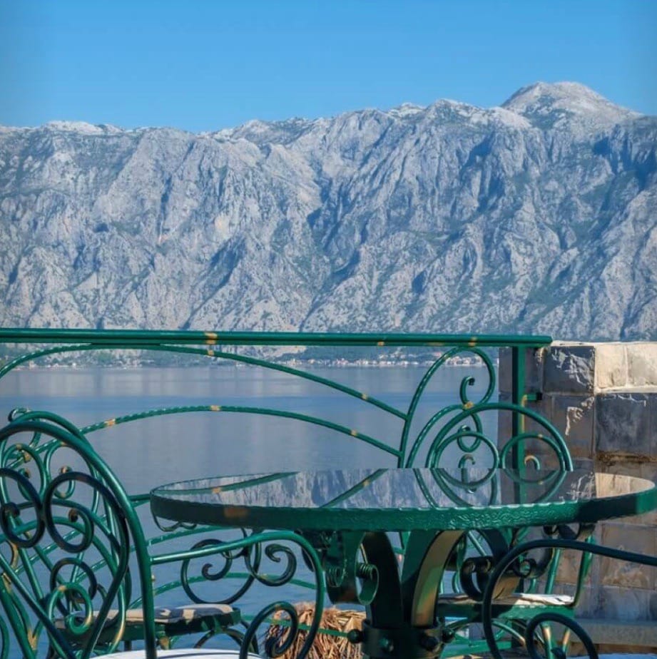 Wrought iron furniture on the terrace of a villa in Stoliv, Montenegro, with a panoramic view of the Bay of Kotor and the mountain landscape.