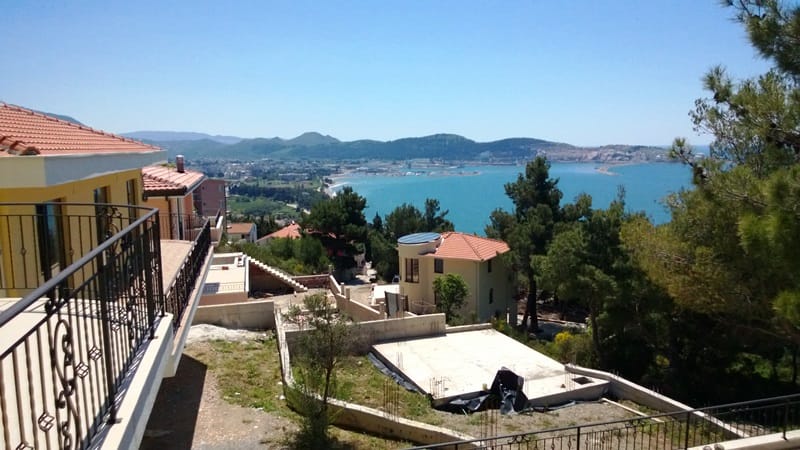 Панорамный вид на море и горы с террасы дома в Шушани, Черногория: черепичные крыши, сосны и морской залив.