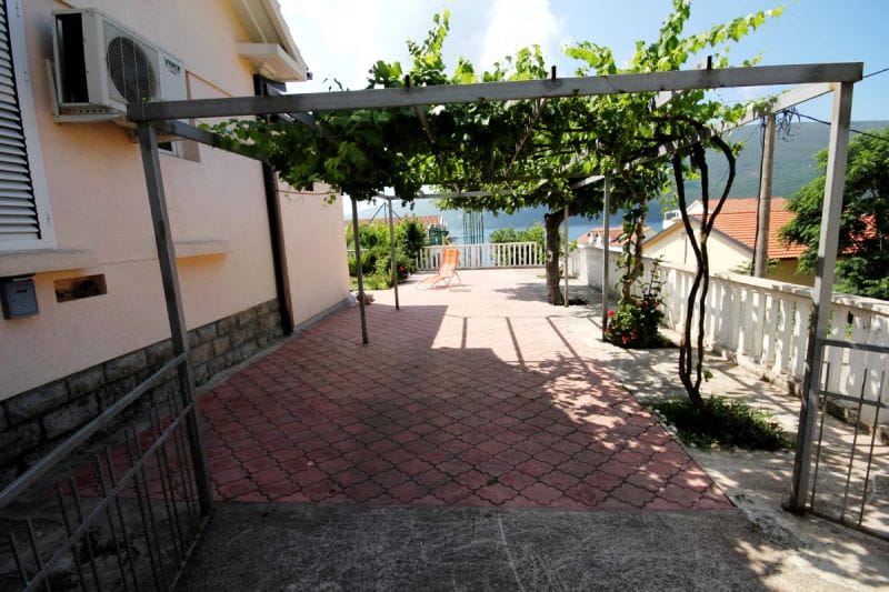 Terasa sa vinovom lozom pored kuće u Đenovićima, Crna Gora: pogled na more, popločano dvorište i prostor za odmor.