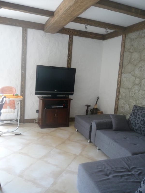 Living room in a villa in Bigovo, Montenegro: interior with wooden beams, a stone wall, a sofa, and a TV area.