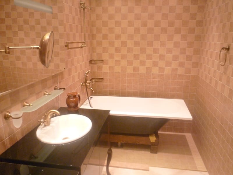 Bathroom in a villa in Bigovo, Montenegro: beige tile, a classic bathtub, and a sink with brass faucets.