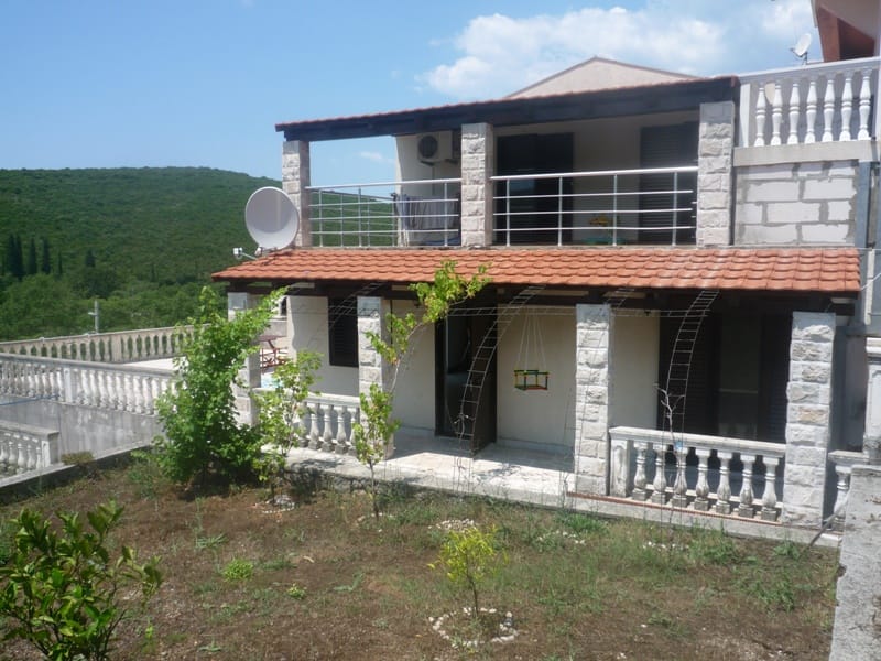 Karadağ, Bigovo'da iki katlı villa: taş kaplama, korkuluklu teraslar, bahçe ve yeşil tepeler manzarası.