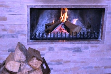 Дровяной камин с отделкой из натурального камня в доме в Игало, Черногория. Уютная гостиная с поленницей дров.