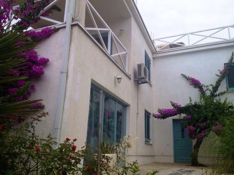 Fasada kuće u Dobrim Vodama, Crna Gora: beli zidovi, balkon s terasom, plave škure i cvetajuća bugenvilija u bašti.