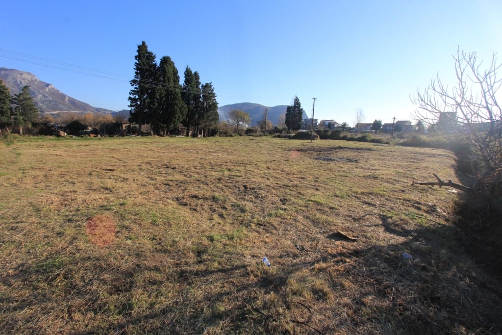 Building plot for sale in Buljarica, Montenegro: flat terrain with mountain and cypress tree views.