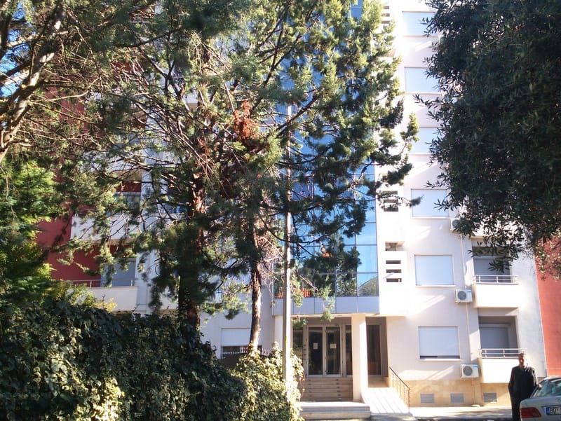 Savremena stambena zgrada sa panoramskim staklenim površinama i zelenim vrtom u Budvi, Crna Gora — pogled na fasadu zgrade.