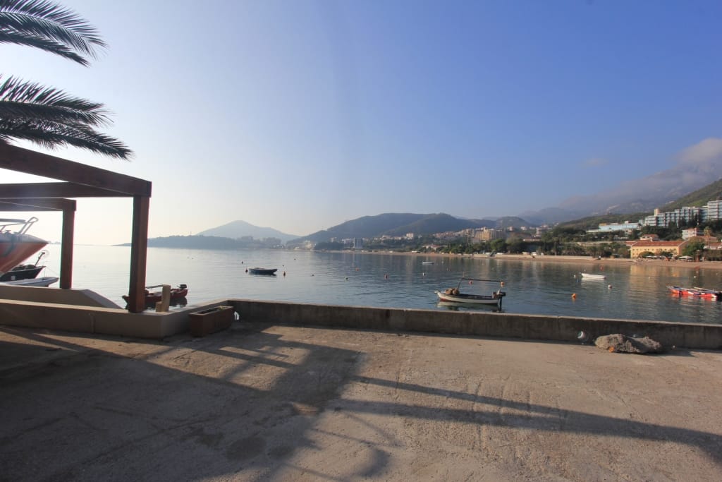 Вид на море и набережную с террасы коммерческого помещения в Рафаиловичи, Черногория, с причалом для лодок.