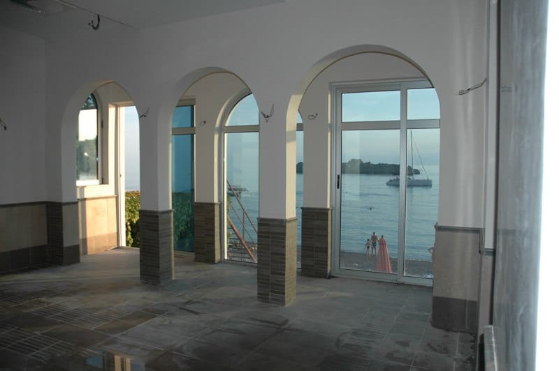 Restaurant interior in Sveti Stefan, Montenegro: panoramic arched windows with sea and beach views, tiled finish.