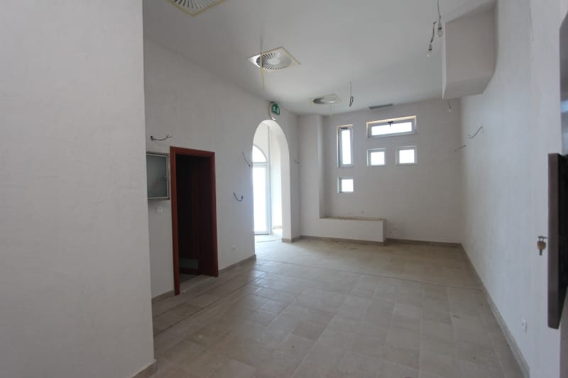 Bright commercial space for a restaurant in Sveti Stefan, Montenegro: white walls, stone floor, and an arched passage.