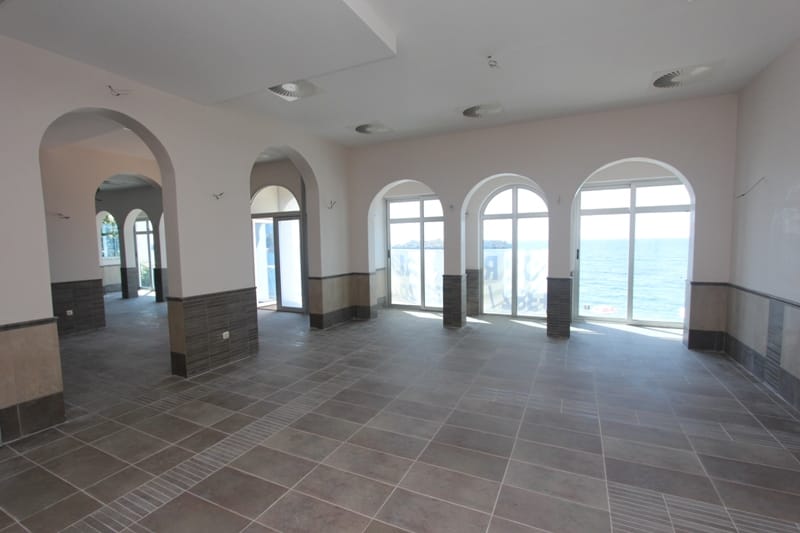 Spacious restaurant hall in Sveti Stefan, Montenegro, with arched windows and panoramic views of the Adriatic Sea.