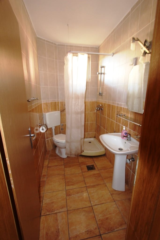 Kupatilo sa tuš kabinom i belom sanitarnom opremom u mini-hotelu, Sutomore, Crna Gora. Završna obrada bež pločicama.