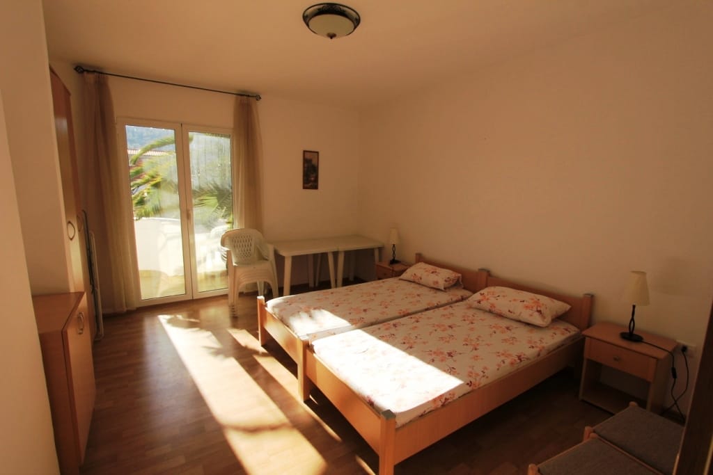 Svetla spavaća soba sa dva kreveta u mini-hotelu, Sutomore, Crna Gora: pogled na terasu i nameštaj od svetlog drveta.