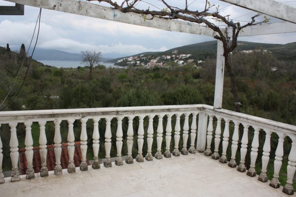 Terrasse avec balustrade offrant une vue sur la mer et les montagnes dans une maison située à Bigovo, Monténégro. Espace extérieur avec une pergola recouverte de vigne.