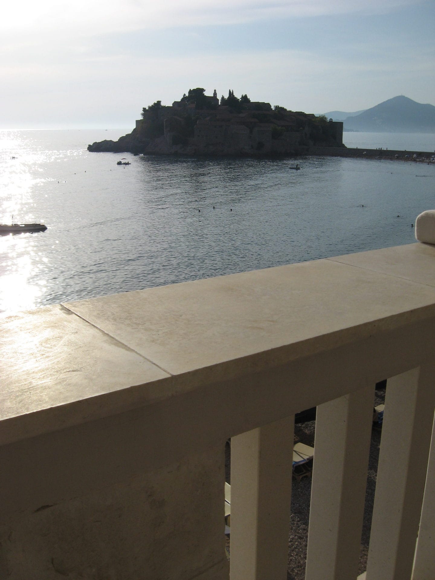 View of Sveti Stefan Island in Montenegro from the balcony of an apartment with stone railings and a sea view.