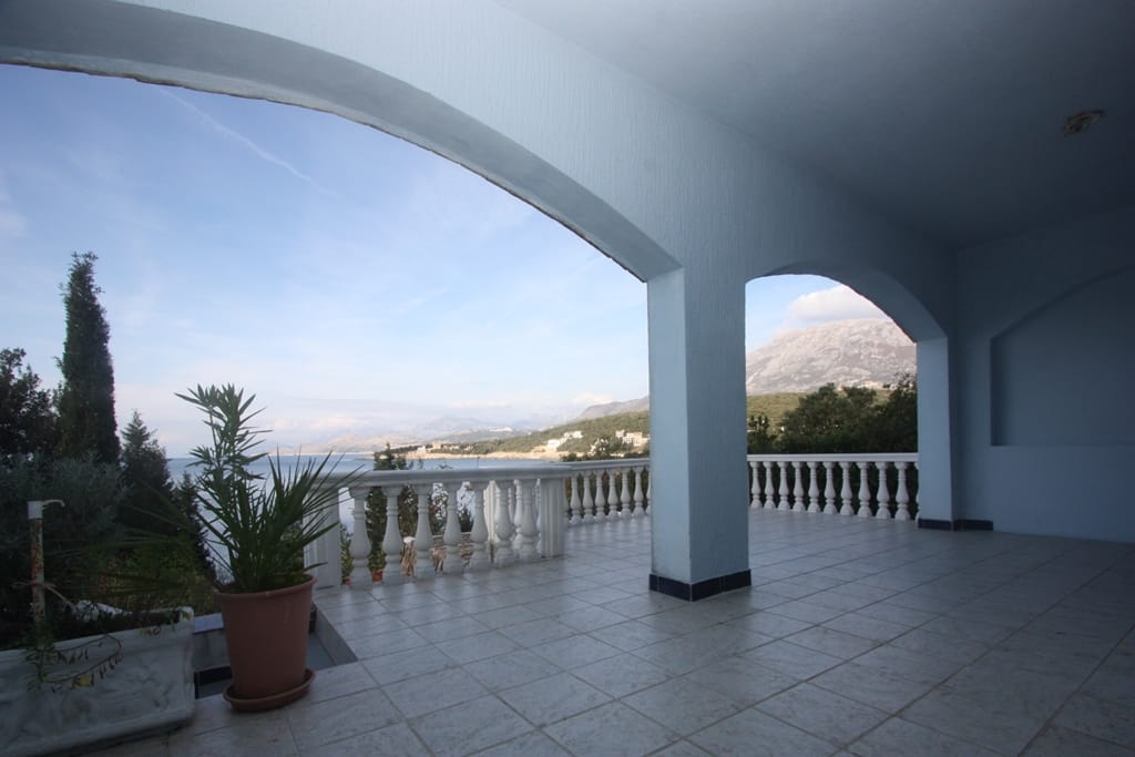 Przestronny taras z balustradą oraz widokiem na morze i góry w domu, Utjeha, Czarnogóra. Podłoga wyłożona płytkami i łukowe otwory.