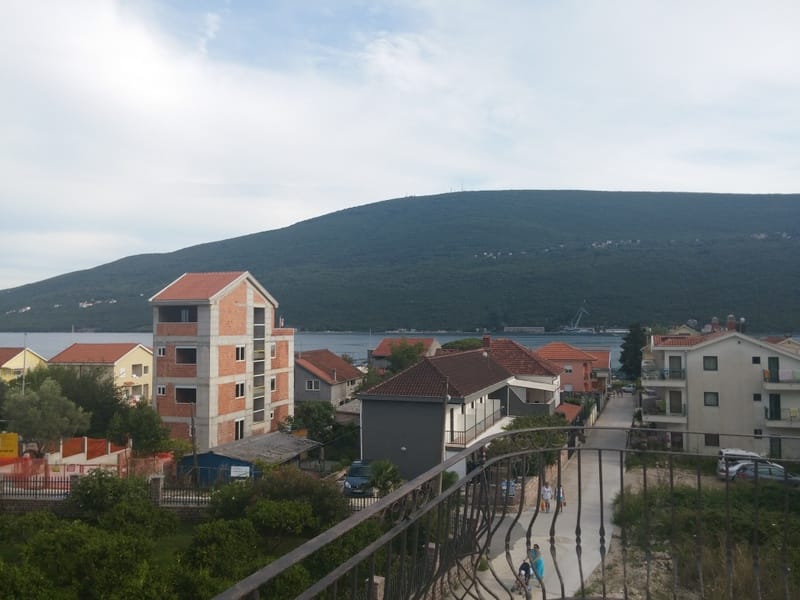 View from the balcony of the sea and mountains in Đenovići, Montenegro: a panorama of the village with houses and a wrought-iron terrace railing.