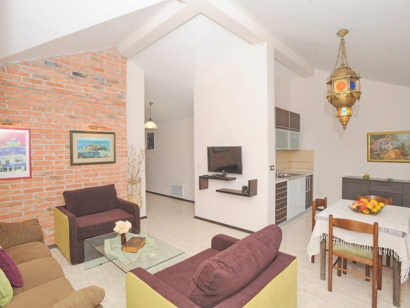 Karadağ, Bigovo'daki bir villada tuğla duvarlı oturma odası ve mutfak iç mekanı: yumuşak mobilyalar, yemek alanı ve dekor.