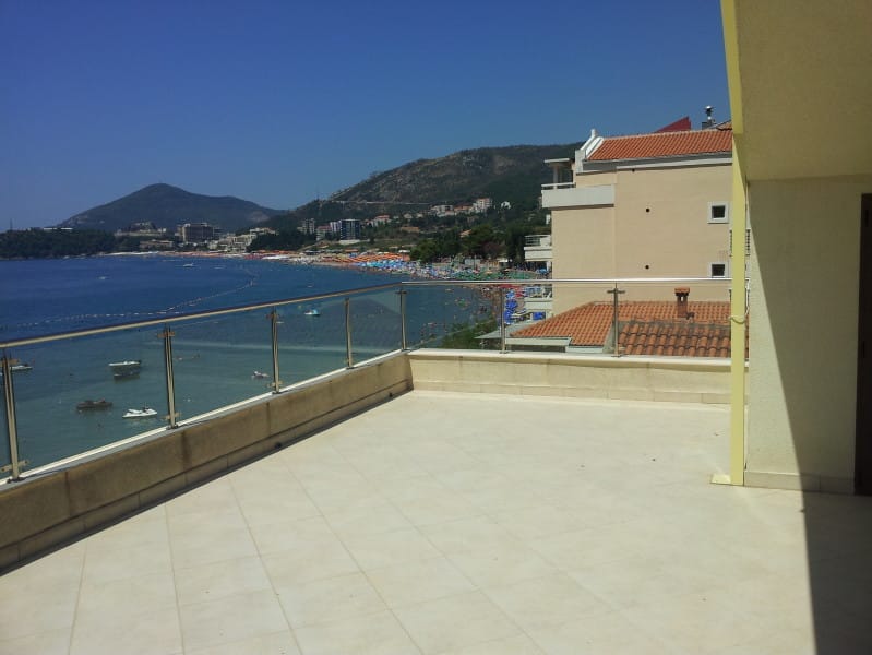 Terrasse spacieuse avec vue panoramique sur la mer et la plage à Rafailovići, Monténégro, dotée d'une balustrade en verre moderne.