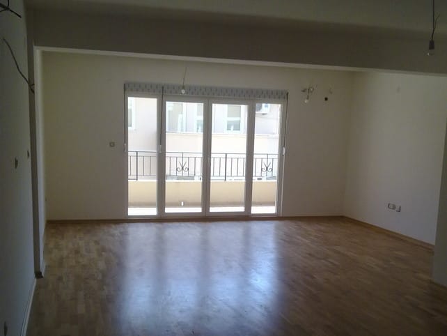 Spacious living room in an apartment in Budva, Montenegro, with parquet flooring, white walls, and access to the balcony.