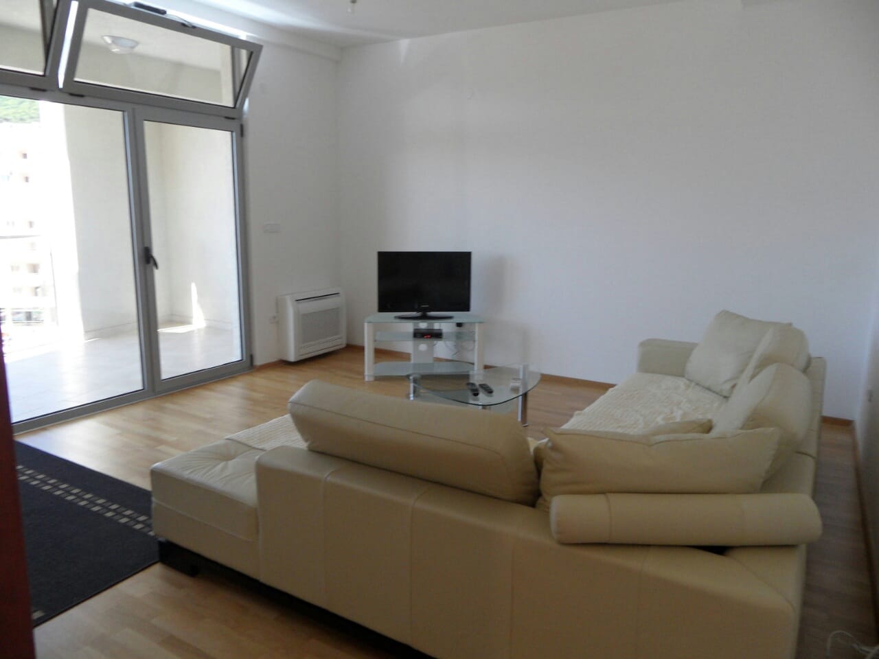 Bright living room with a leather sofa and terrace access in an apartment in Budva, Montenegro. Modern interior with a TV.