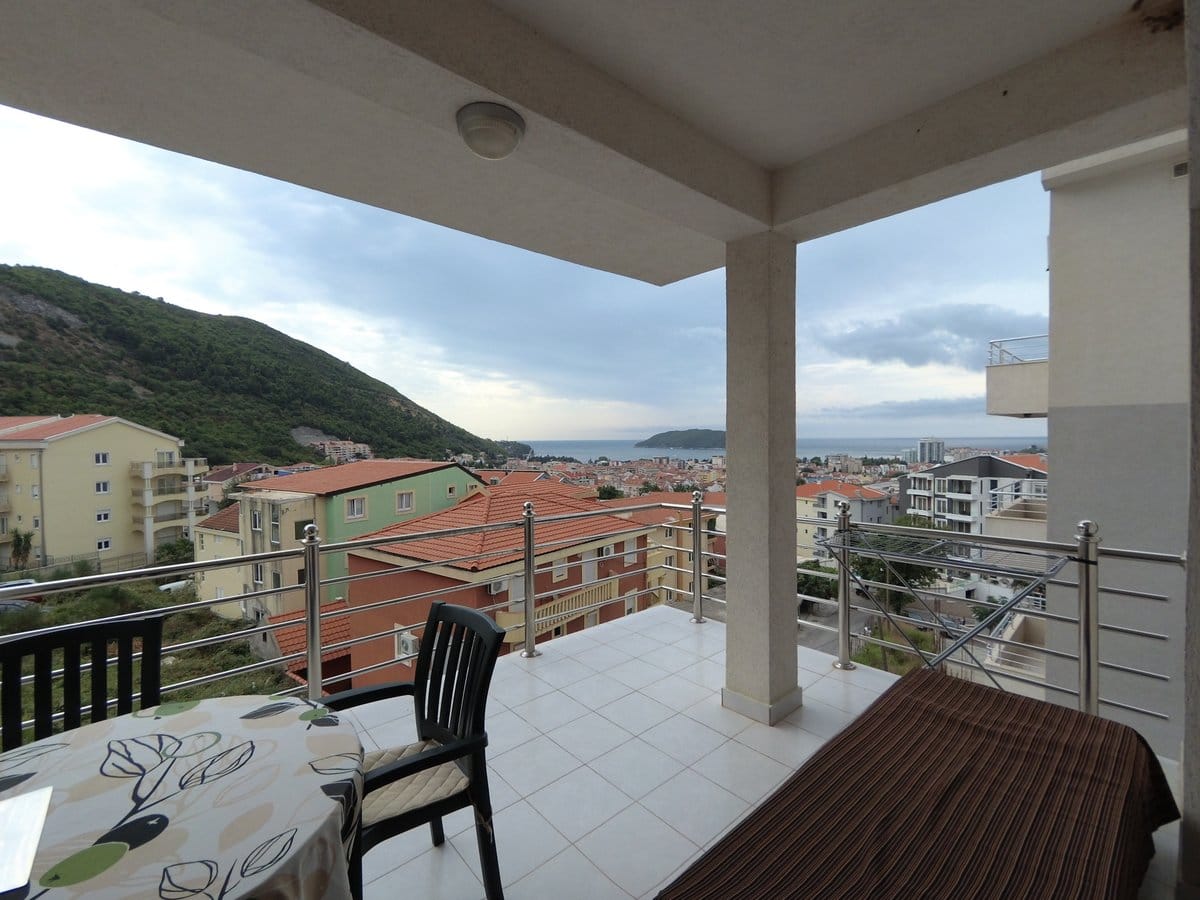 Prostrana terasa s pogledom na more i planine u stanu, Budva, Crna Gora: pločice na podu, trpezarijski deo i ograda.