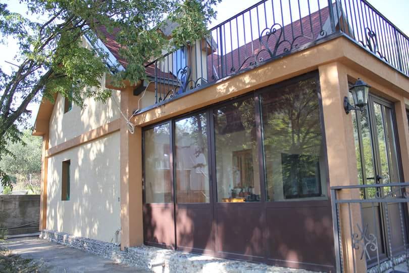 Two-story house in Sutomore, Montenegro, featuring panoramic windows, a terrace, and wrought-iron railings on the second floor.