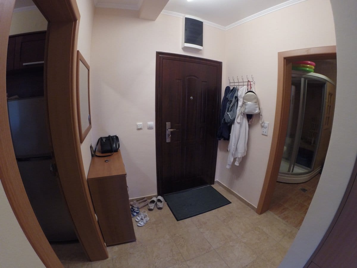 Прихожая в квартире в Баошичи, Черногория: темная входная дверь, комод, вешалка для одежды и вид на душевую кабину.