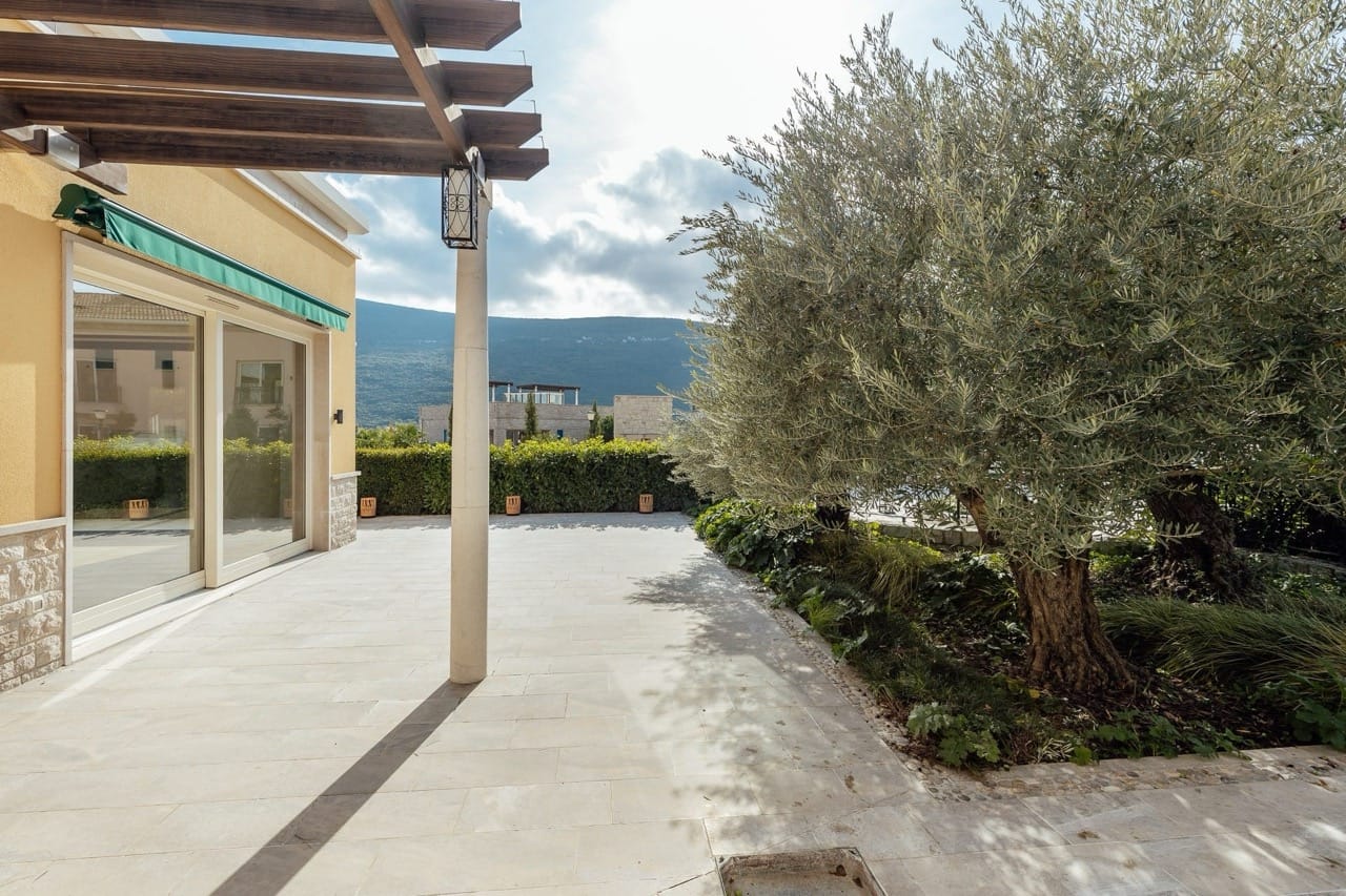 Villa terrace in Portonovi, Kumbor, Montenegro: stone paving, wooden pergola, olive tree, and mountain view.