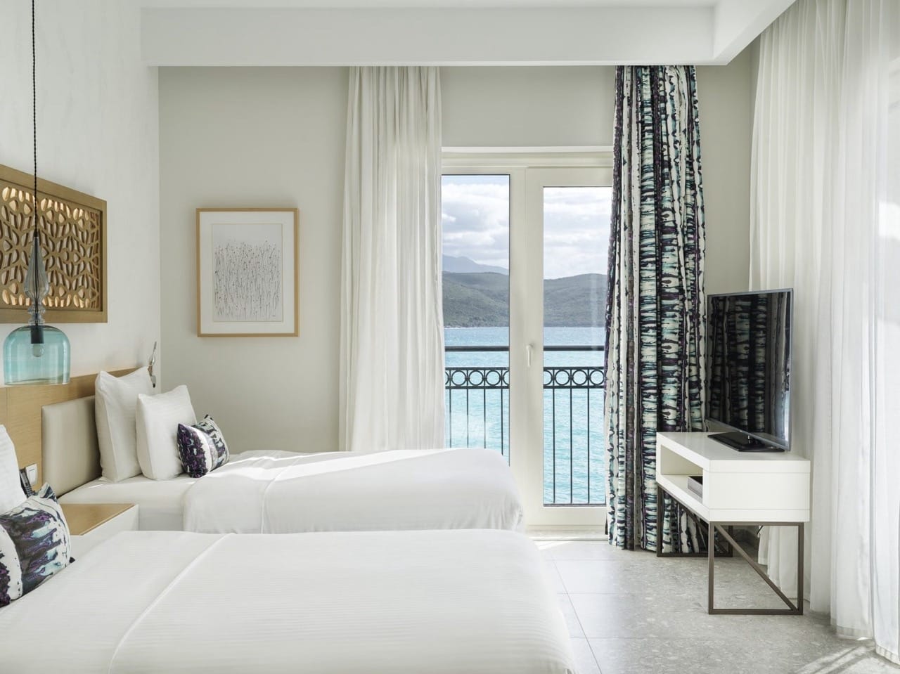 Спальня в апартаментах Lustica Bay, Радовичи, Черногория: две кровати, современная мебель и вид на море с балкона.