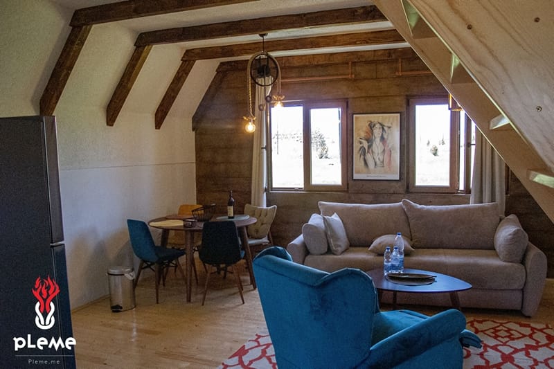 Salon w drewnianym stylu z belkami w kompleksie domów, Žabljak, Czarnogóra: miękka sofa, fotel i jadalnia.