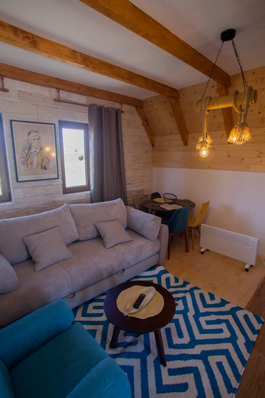 Przytulny salon w drewnianym domu w Žabljaku, Czarnogóra: miękka sofa, stylowy wystrój, belkowany sufit i widok na góry.