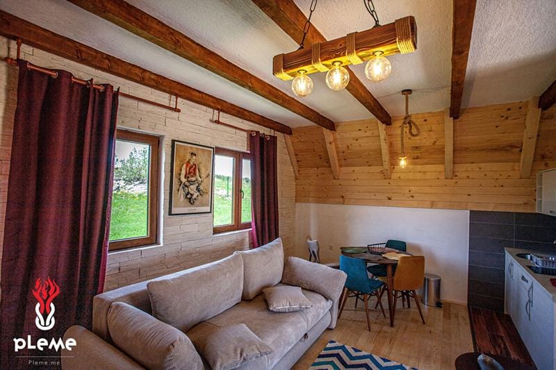 Salon w stylu rustykalnym z drewnianymi belkami w domu, Žabljak, Czarnogóra: miękka sofa, jadalnia i widok na góry.