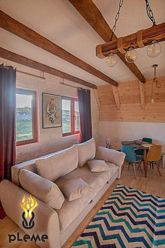 Salon w stylu rustykalnym z drewnianymi belkami w domu, Žabljak, Czarnogóra: miękka sofa, jadalnia i widok z okien.
