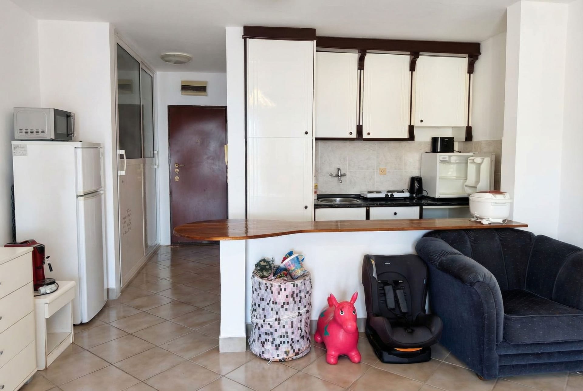 Kitchen-living room with a bar counter in an apartment in Sveti Stefan, Montenegro: white cabinets, tiled floor, and upholstered furniture.