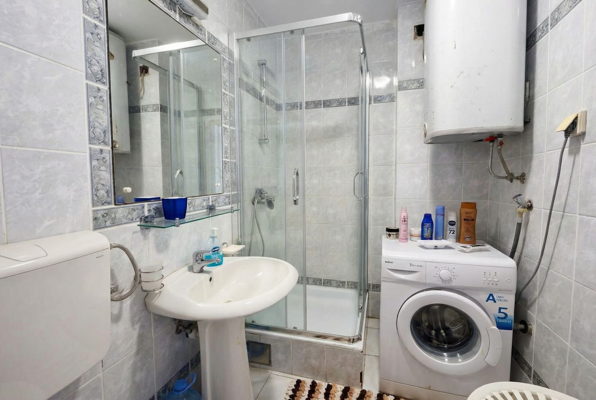Bathroom in an apartment in Sveti Stefan, Montenegro: shower cabin, sink, mirror, and washing machine.