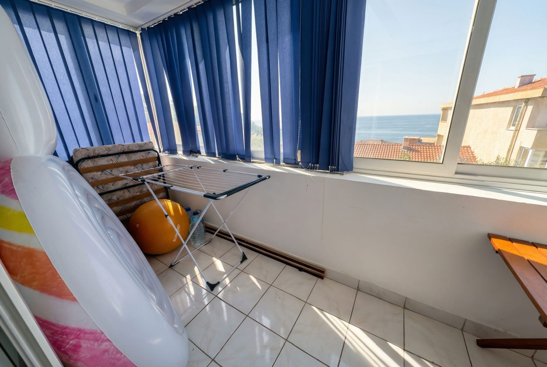Apartment balcony in Sveti Stefan, Montenegro, with panoramic sea view, blue blinds, and a floor clothes drying rack.