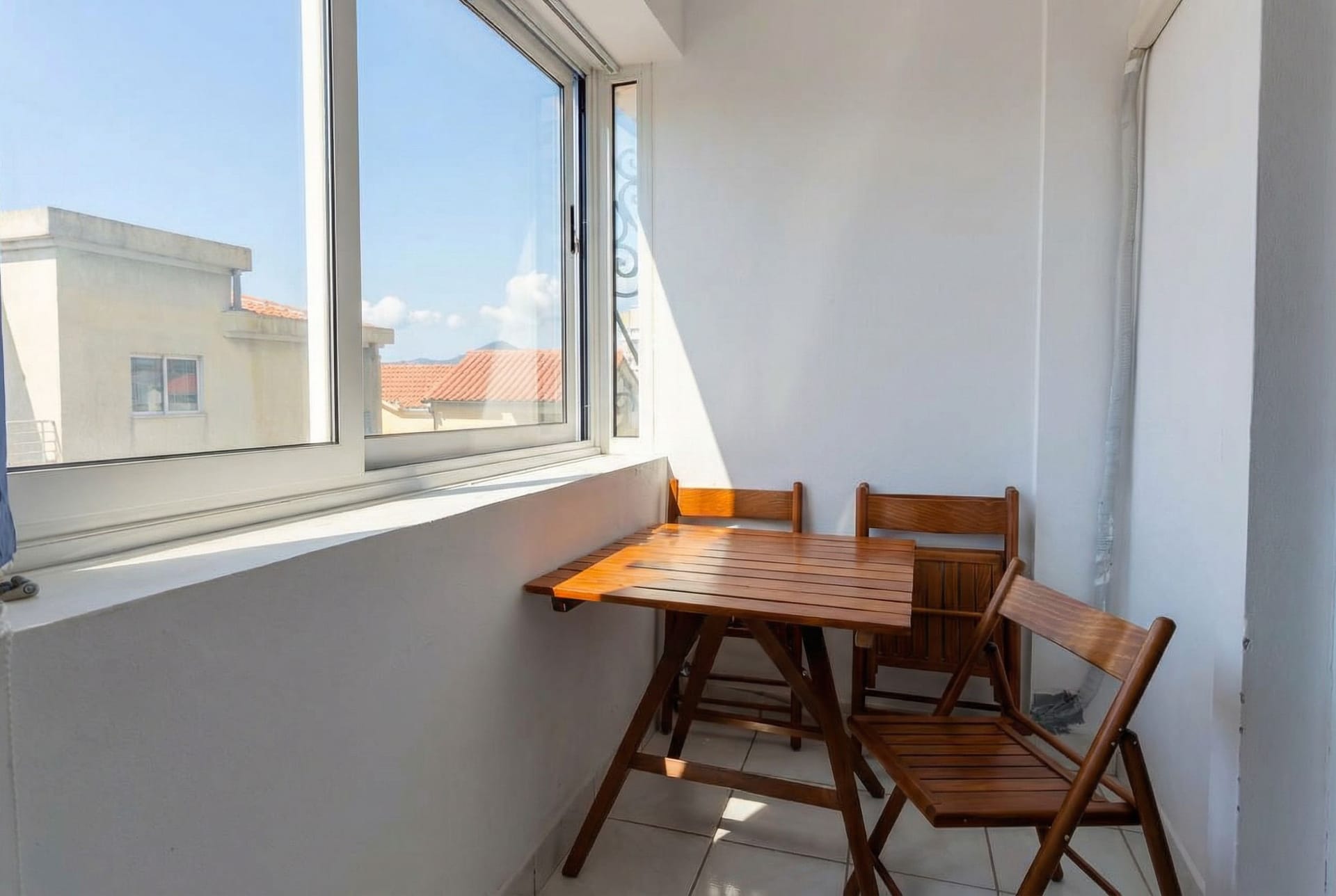 Bright balcony with wooden furniture and a view of tiled roofs in an apartment, Sveti Stefan, Montenegro.