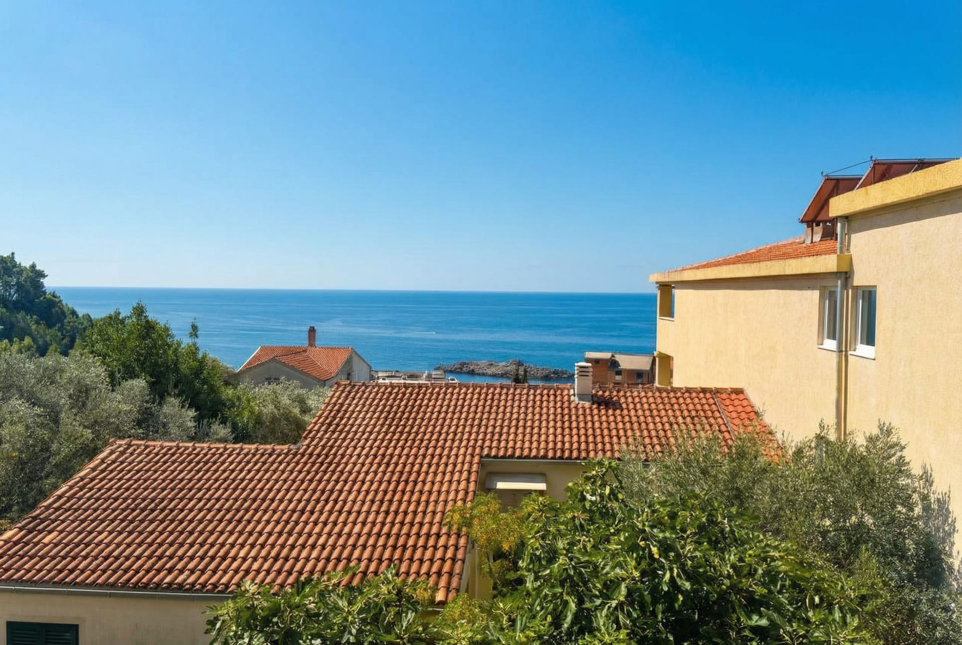 Sea view and tiled rooftops in Sveti Stefan, Montenegro, a panoramic view of the coast from the apartment terrace.