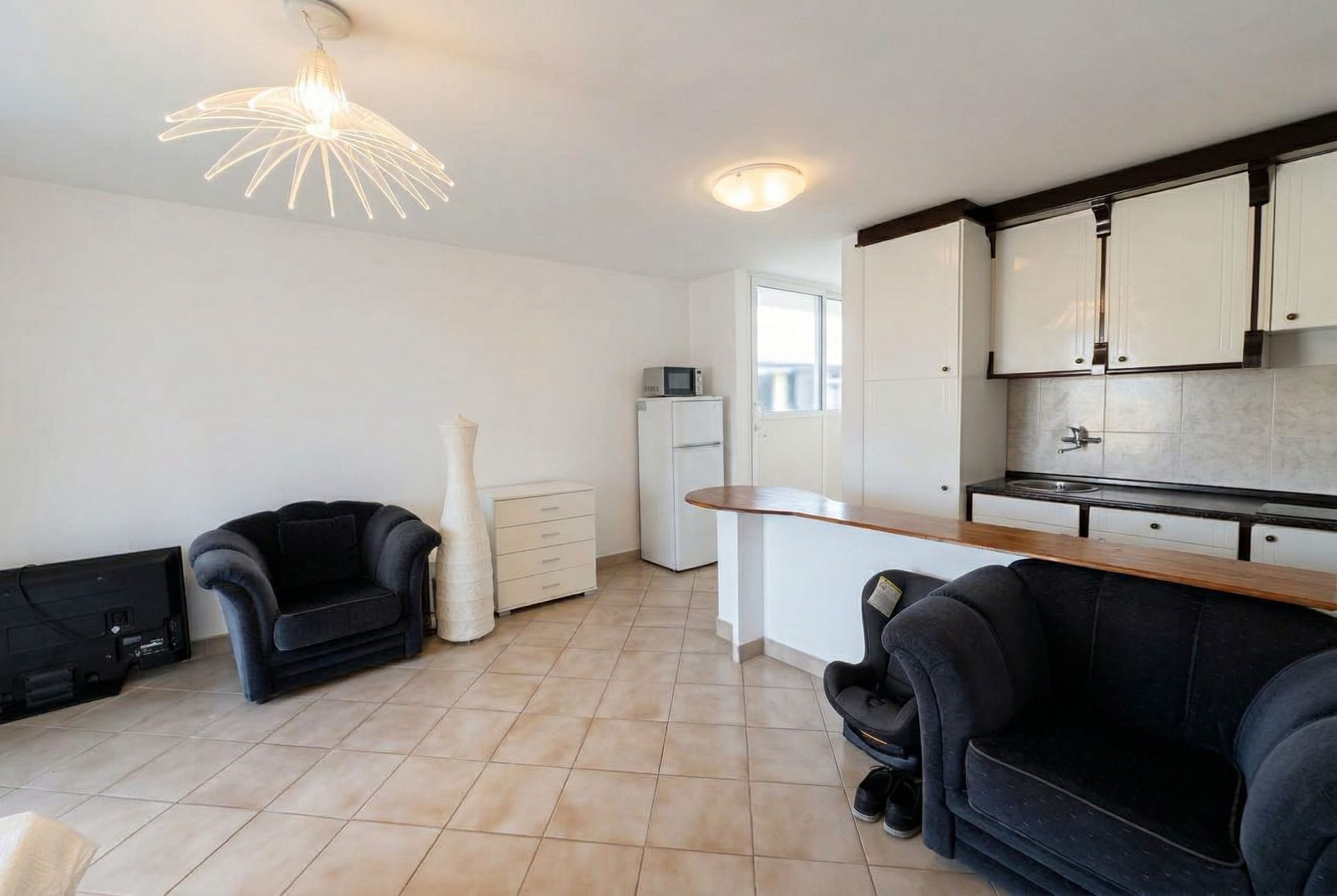 Living room with kitchen in an apartment in Sveti Stefan, Montenegro: soft seating, a breakfast bar, and light floor tiles.