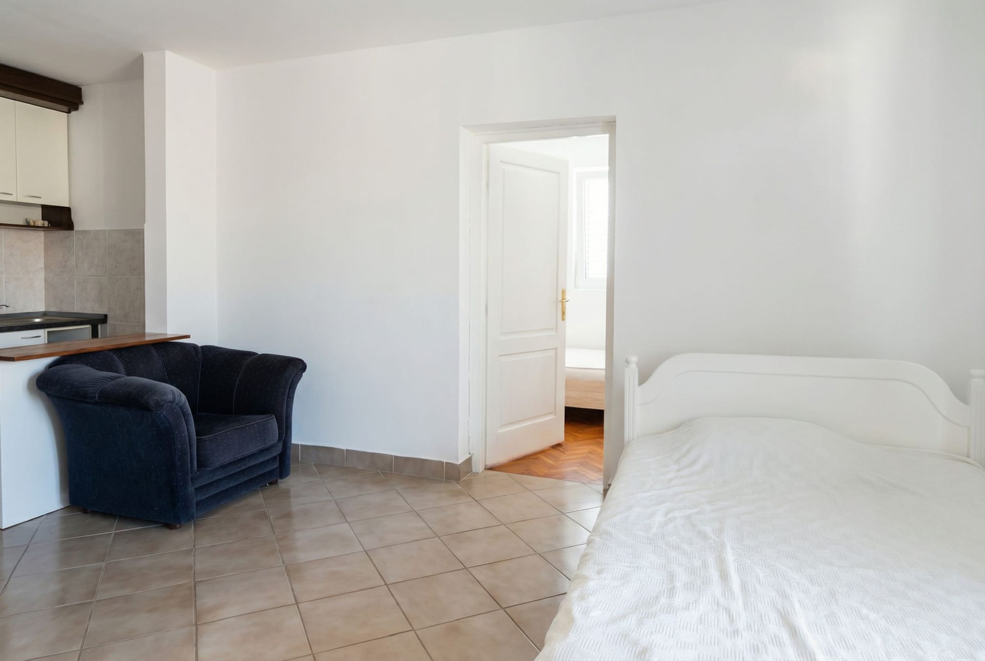 Living room interior with kitchen and sleeping area in an apartment, Sveti Stefan, Montenegro: white furniture and tiled floor.