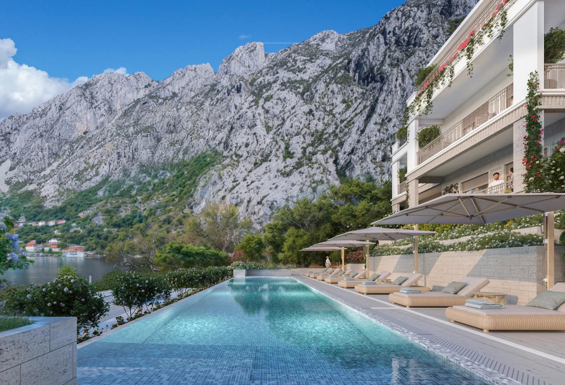Piscine avec chaises longues dans un complexe résidentiel à Luštica, Monténégro, avec les montagnes et le littoral en arrière-plan.