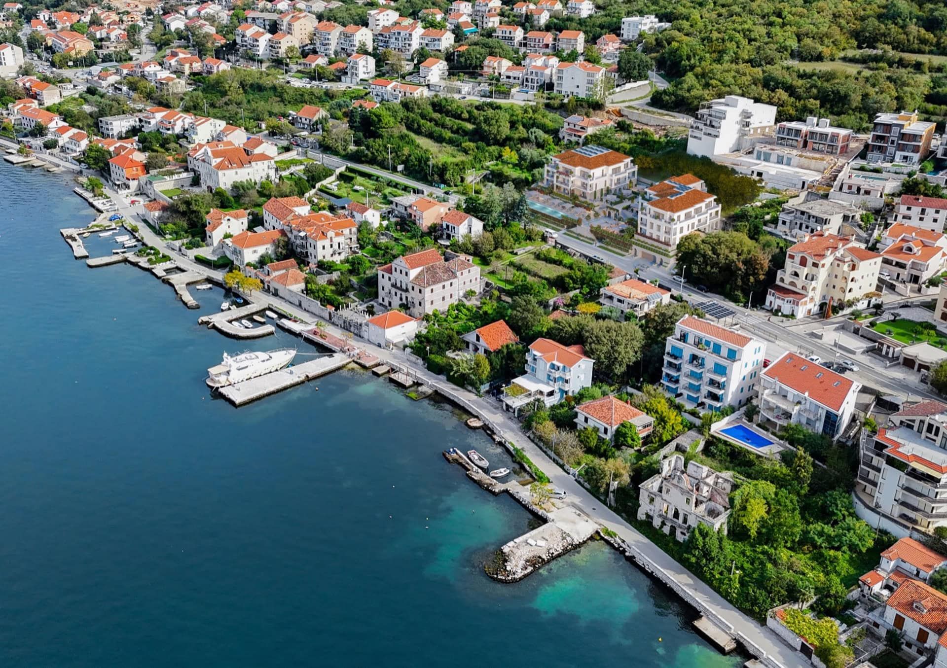 Vue aérienne d’un complexe résidentiel à Ljuta, Monténégro : maisons côtières aux toits rouges et quais privés en bord de mer.