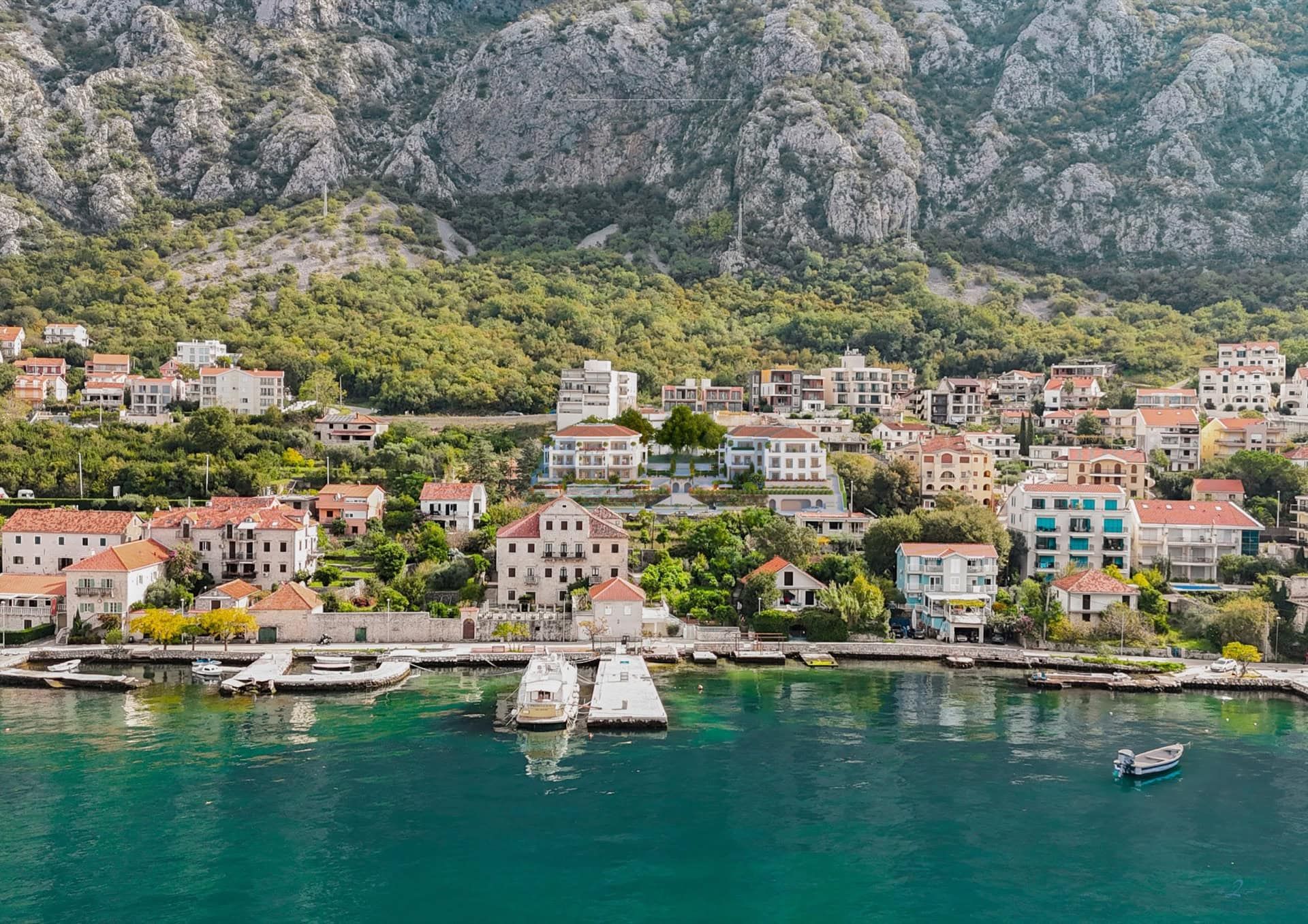 Vue depuis la mer sur un complexe résidentiel à Ljuta, Monténégro : maisons côtières aux toits de tuiles, montagnes et ponton privé.
