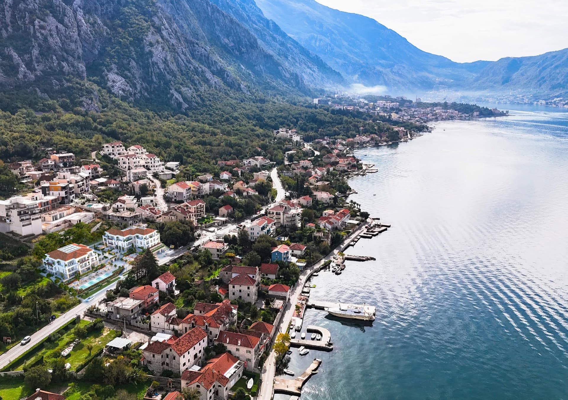 Vue panoramique sur un complexe résidentiel à Ljuta, Monténégro : bâtiments modernes en bord de mer avec piscine et paysage montagneux.